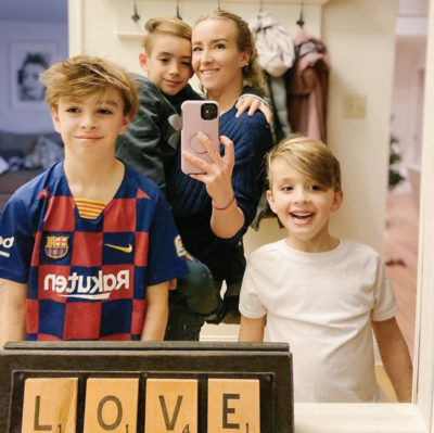 Blonde woman standing in front of mirror with three children, sign at the bottom of the mirror says "LOVE" in scrabble-type letters
