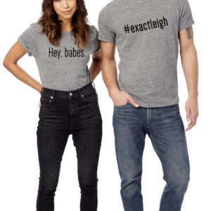 A brunette woman and a sandy haired man, both wearing jeans and grey t-shirts. Her shirt says, Hey, babes. His shirt says #exactleigh.