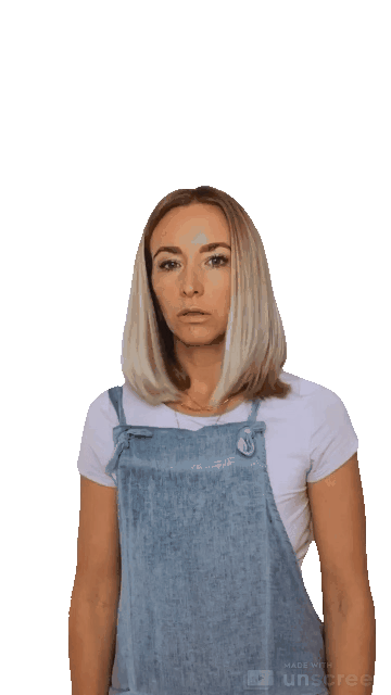 Animated gif of a blond woman with a pale purple shirt and denim overalls looks left then right, points to herself, mouths "Who, me?" and shakes her head no